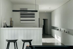 A modern kitchen with a white countertop, two black bar stools, and a hanging light fixture. - Her Huahin Pool Villa (Hua Hin)