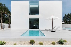 Un bâtiment moderne doté d’une piscine, de chaises longues et d’un parasol blanc.
