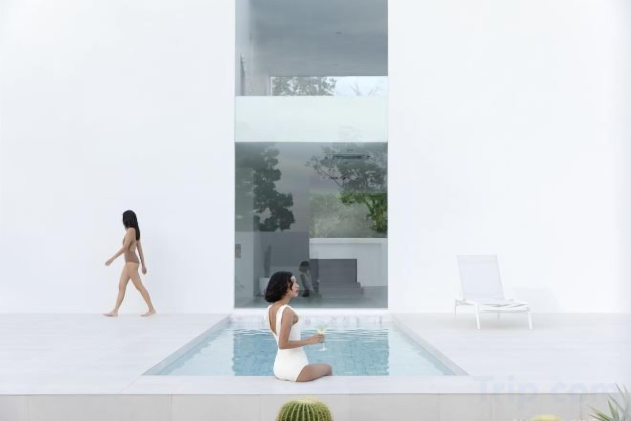 Un espace piscine intérieur moderne, doté d’un mur en verre, d’une chaise longue et d’une personne assise au bord de la piscine.