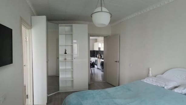 Ein Schlafzimmer mit Bett, Kleiderschrank und einem zur Küche hinführenden Flur.