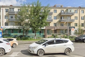 Un edificio de varios pisos con balcones, un árbol en primer plano y coches aparcados.