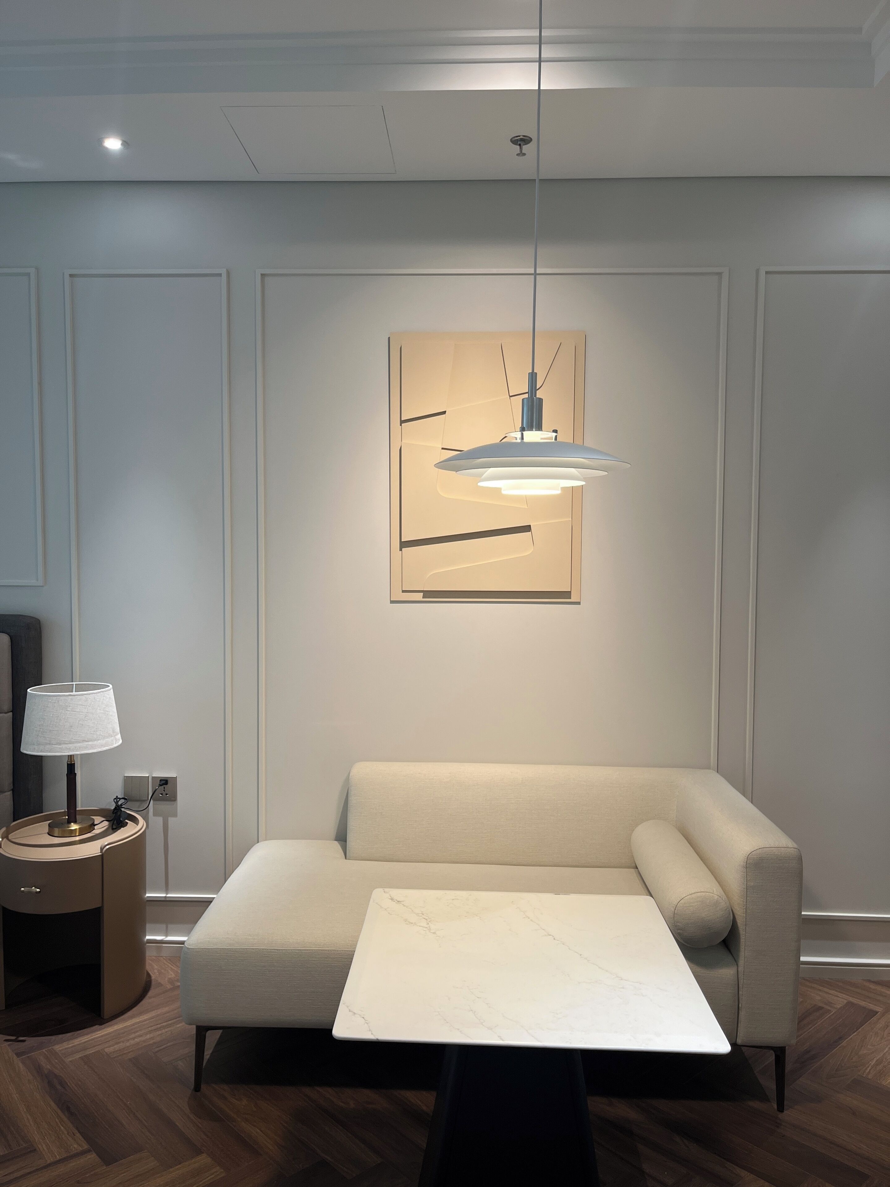 Uma sala de estar moderna com um sofá, uma mesa, um abajur e uma luminária pendente.