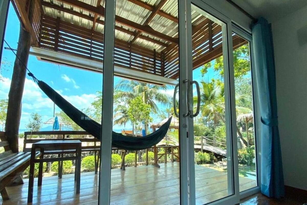 A room with a large sliding glass door leading to an outdoor deck with a hammock, wooden furniture, and a view of palm trees.
