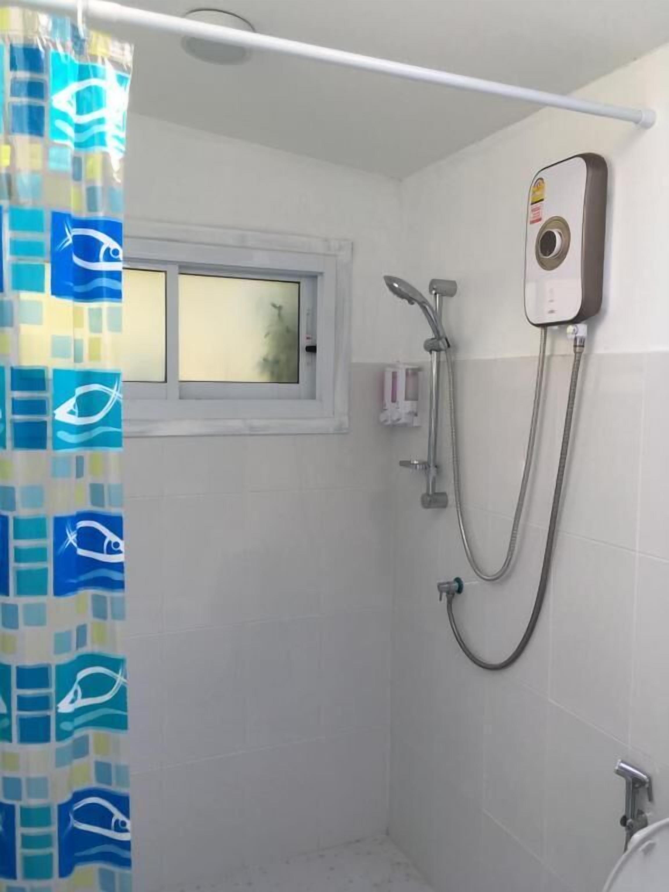 A small bathroom with a shower, a window, and a curtain with a fish pattern.