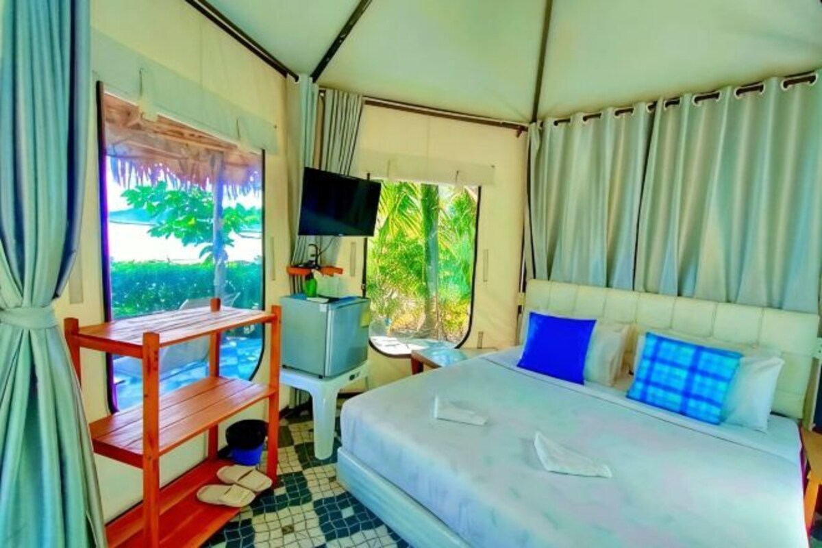 A tent-style room with a bed, a desk, a TV, and a window with curtains.