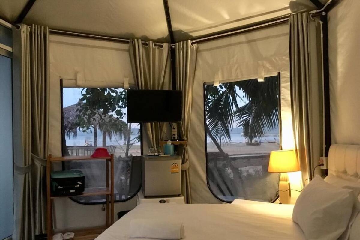 A hotel room with a bed, a TV, a shelf with luggage, and a view of palm trees.