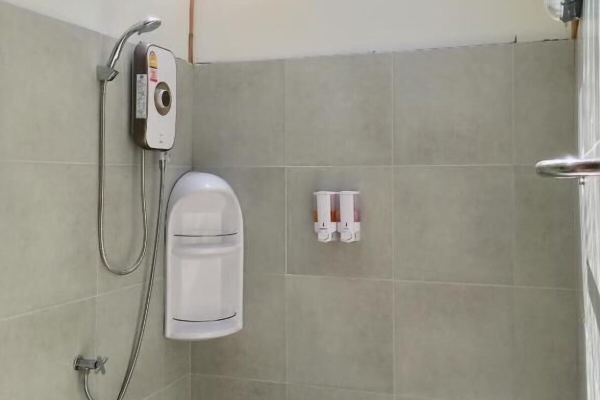 A shower area with a glass ceiling, a handheld showerhead, a wall-mounted soap dispenser, and a water bottle.