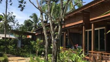 Een tropisch resort met een pad van steen dat leidt naar houten gebouwen, omringd door weelderige begroeiing en palmbomen.
