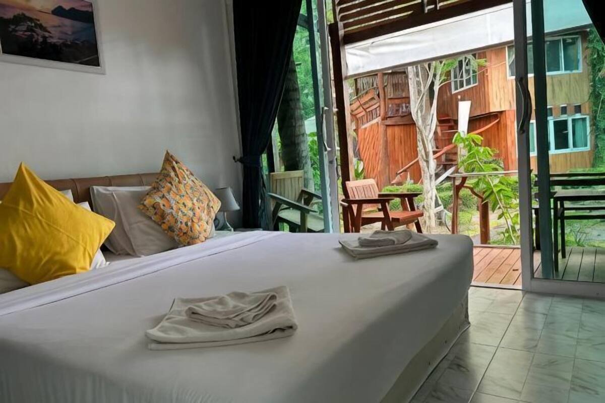 A bedroom with a bed, pillows, a neatly made bed, a window, and an outdoor area with a wooden deck and chairs.