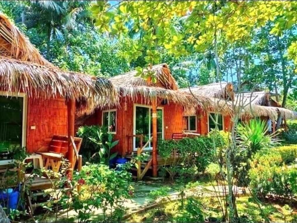 Una cabaña con techo de paja y fachada de madera, rodeada de abundante vegetación.