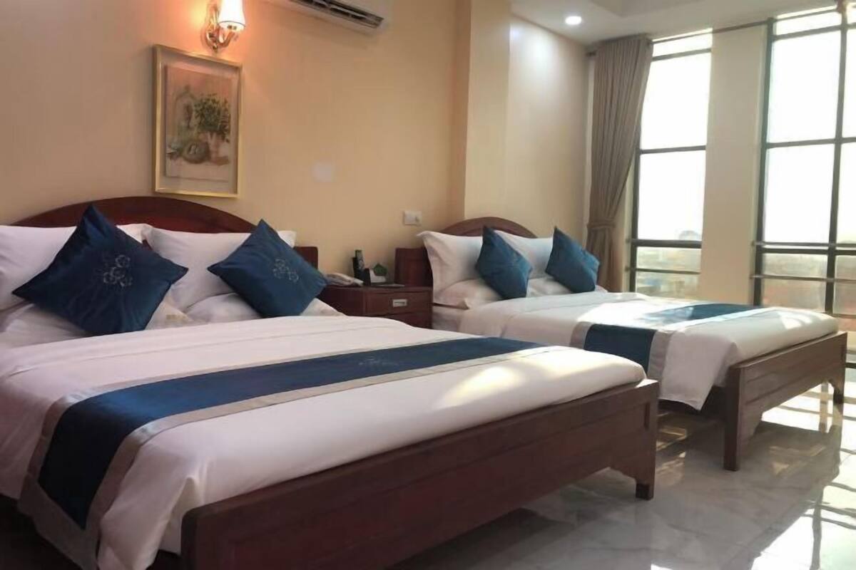 A hotel room with two beds, a nightstand, a lamp, a framed picture on the wall, and a large window with curtains.