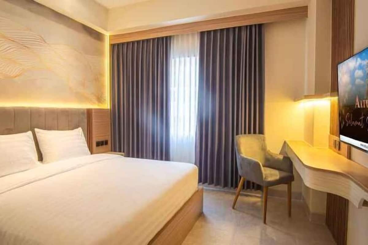 A hotel room with a bed, a desk, a chair, a TV, and a large window with curtains.