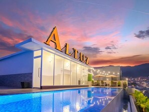 A hotel with a pool, a large illuminated 'A' sign, and a view of the city at dusk.