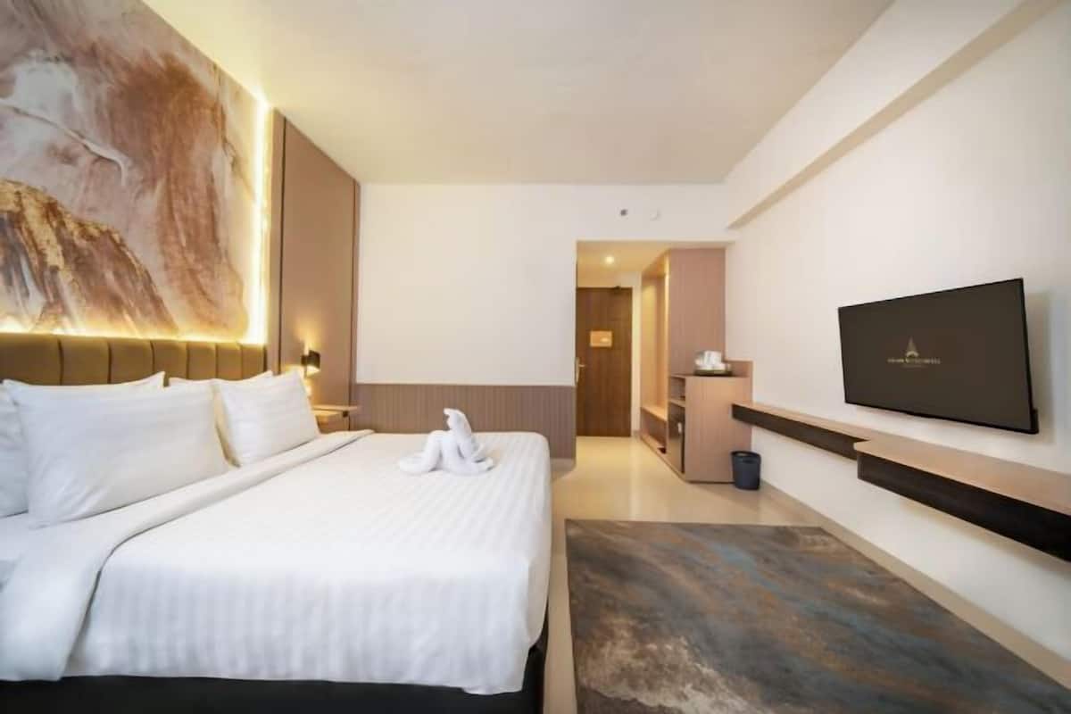 A modern hotel room with a large bed, a flat-screen TV mounted on the wall, and a painting above the bed.