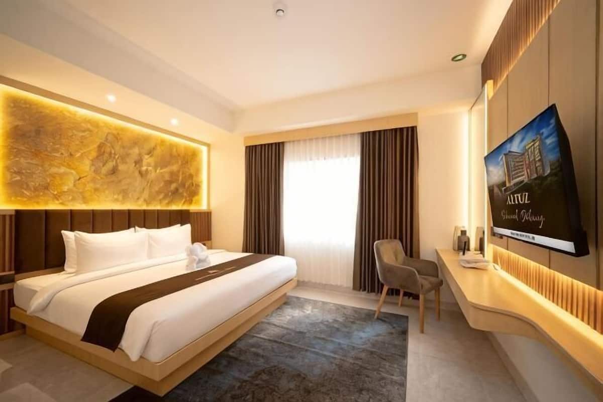 A hotel room with a large bed, a desk with a chair, a flat-screen TV, and a large artwork on the wall.