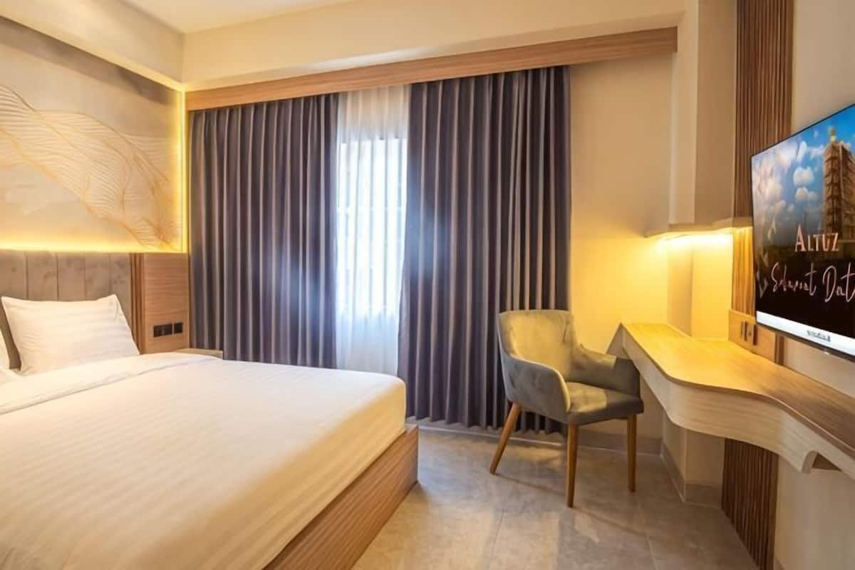 A hotel room with a large bed, a desk with a chair, a TV, and a window with curtains.