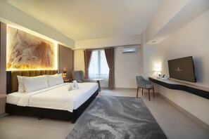 A modern hotel room with a large bed, a desk, a chair, a flat-screen TV, and a wall-mounted air conditioner. - Grand Altuz Yogyakarta (Depok)