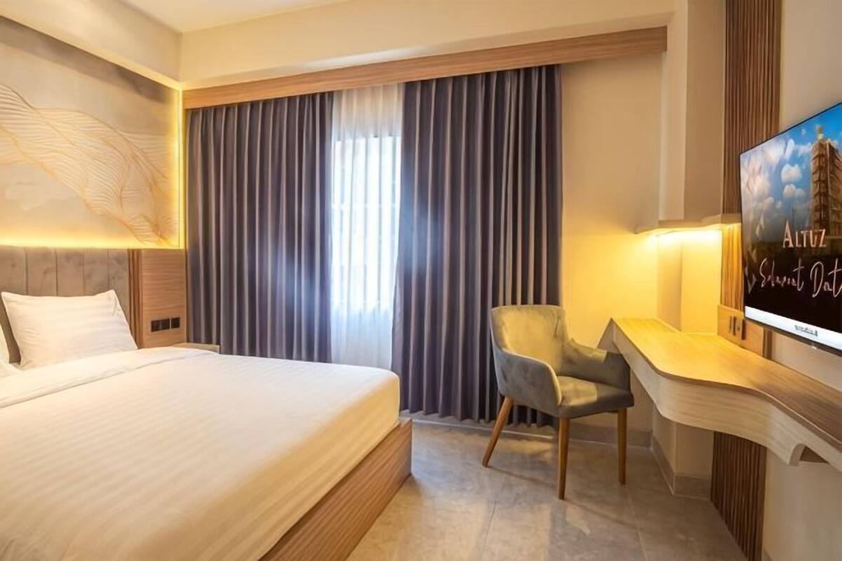 A hotel room with a large bed, a desk with a chair, a TV, and a window with curtains.