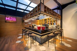 A bar area with a neon sign, wooden shelves, and a bar counter with stools. - Grand Altuz Yogyakarta (Depok)