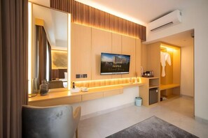 A modern hotel room with a large mirror, a flat-screen TV, a wooden vanity, and a walk-in closet. - Grand Altuz Yogyakarta (Depok)
