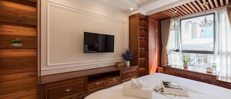 A hotel room with a large bed, a flat-screen TV mounted on the wall, wooden paneling on the walls, a window with curtains, and a ceiling fan.