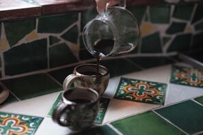 Une main verse un liquide dans une tasse posée sur une surface carrelée à motifs verts et blancs.