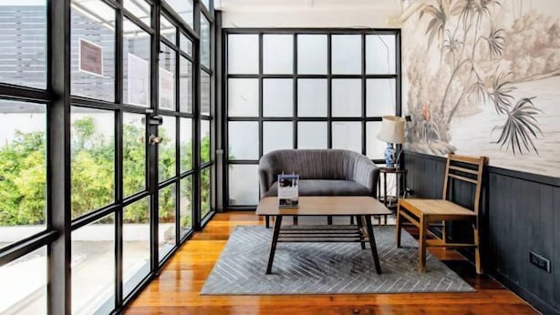 A room with large windows, a gray sofa, a wooden table, and a wall with a floral mural.