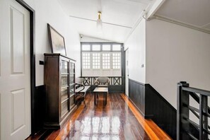 Un pasillo con piso de madera, una escalera, vista al exterior y una puerta a la izquierda.