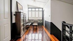 A hallway with wooden flooring, a black railing, a window with white shutters, and a door.