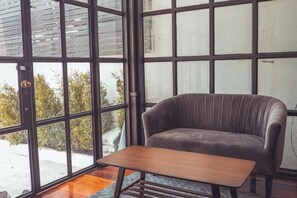 A room with a leather sofa and a wooden table, large windows with a view of greenery outside. - Haheng House (Bangkok)