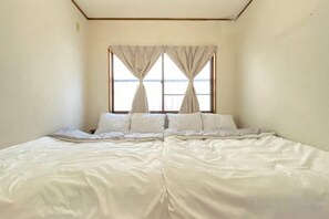 Una cama individual con ropa de cama blanca en una habitación con un ventanal y cortinas.