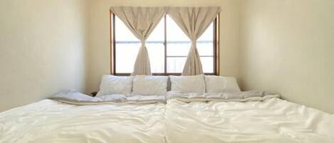 A bedroom with a large bed, a window with curtains, and a plain wall.