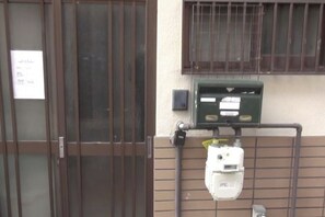 Una entrada de edificio con una reja de metal, una ventana con barrotes y un cuadro eléctrico fijado a la pared.