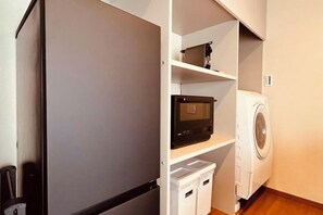 A compact kitchen with a refrigerator, microwave, and washing machine. - HAKUKOU UROMURO (Kyoto)