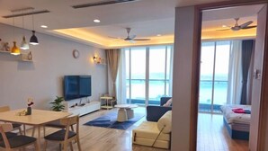 A modern hotel room with a dining area, a sofa, a TV, and a balcony with a view of the sea. - Seaview-Pinetree Marina Resort 2BR [Puteri Harbour] - 5 mins to Legoland (Iskandar Puteri)
