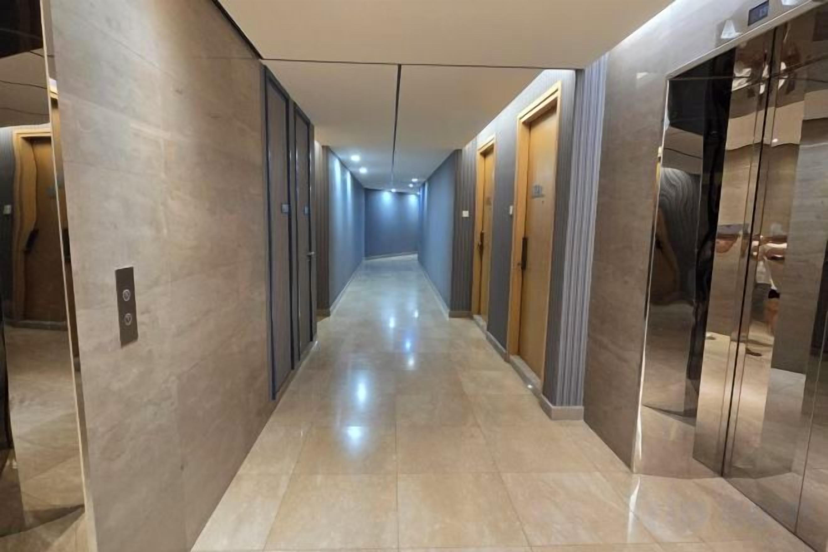 A hotel corridor with a reflective floor, doors on both sides, and an elevator on the right.