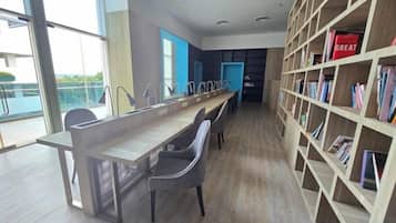 Uma biblioteca moderna com uma mesa comprida e cadeiras, uma estante e vista através de amplas janelas.