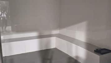 A bathroom with a bathtub, a shower area, and a small shelf with a black object on it.