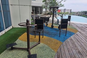 An outdoor exercise area with a wooden deck, exercise equipment, and a pool in the background. - Seaview-Pinetree Marina Resort 2BR [Puteri Harbour] - 5 mins to Legoland (Iskandar Puteri)