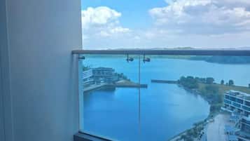 A balcony with a glass railing overlooking a body of water, buildings, and a clear sky.