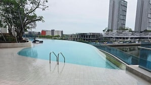 A swimming pool with a curved edge, surrounded by a tiled deck and a wooden walkway. - Seaview-Pinetree Marina Resort 2BR [Puteri Harbour] - 5 mins to Legoland (Iskandar Puteri)