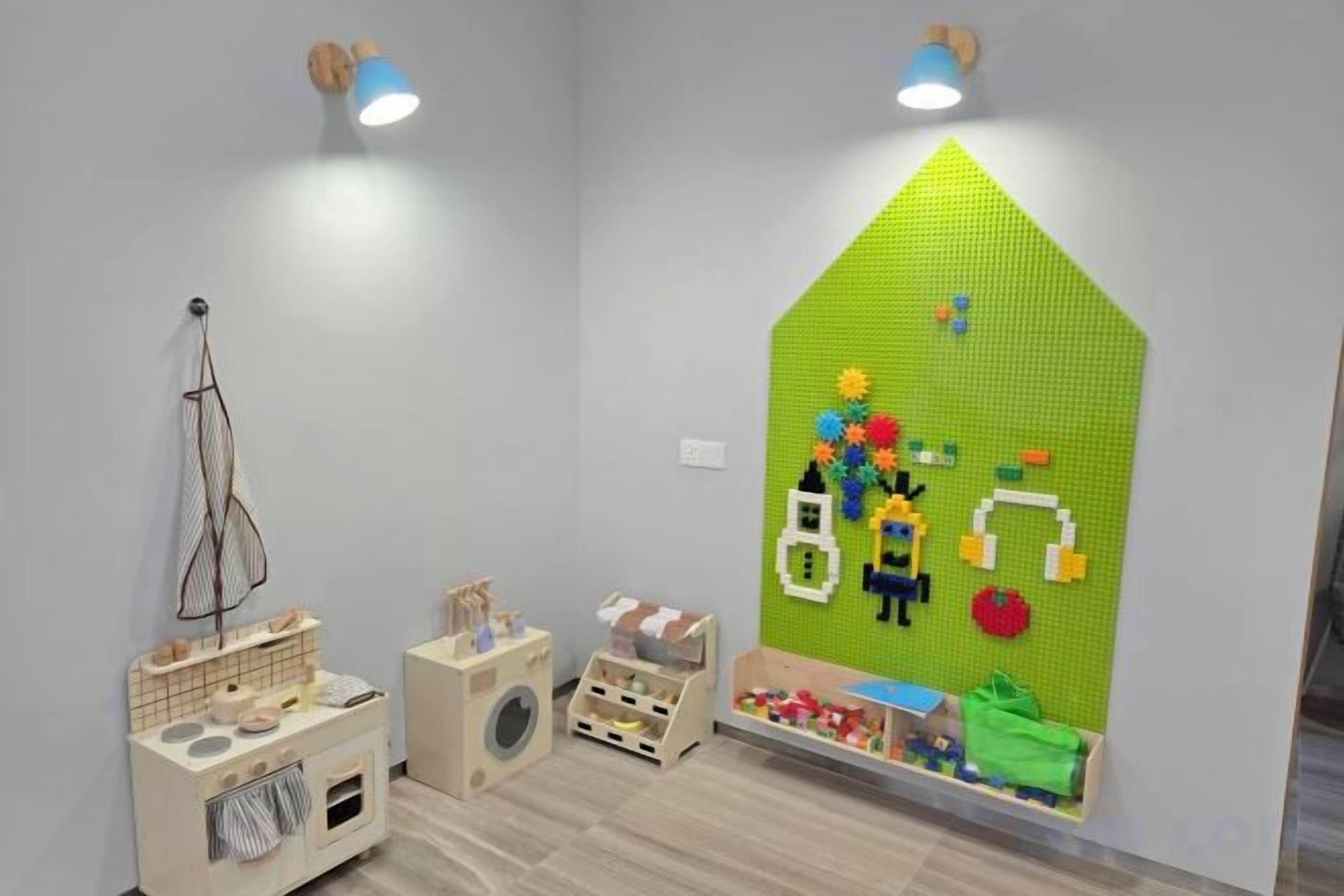 A playroom with a green wall decoration, wooden playpen, and a hanging toy rack.