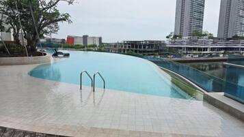 Une piscine à bord incurvé, une terrasse en bois et une vue sur les grands immeubles qui se dressent à l’arrière-plan.