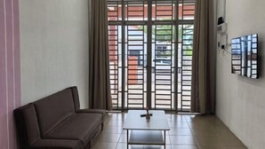 A room with a sofa, a small table, a TV mounted on the wall, and a sliding glass door leading to an outdoor area. - Homestay Sungai Karangan Near Inokom (Padang Meha)