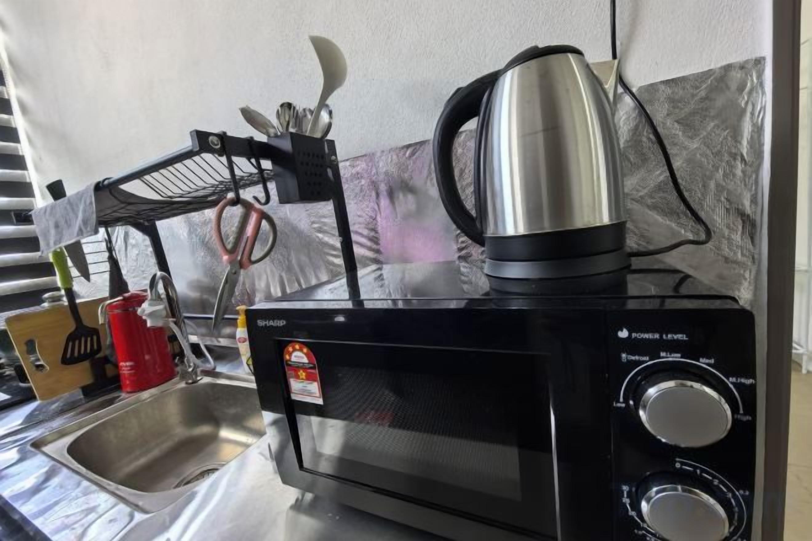 A kitchen with a microwave, kettle, and a sink.