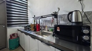 A kitchen with a stainless steel sink, a kettle, and a gas cylinder. - Homestay Sungai Karangan Near Inokom (Padang Meha)