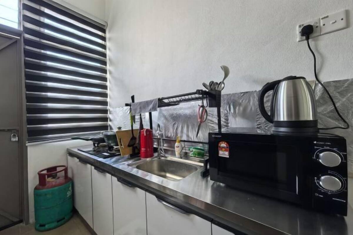 A kitchen with a stainless steel sink, a kettle, and a gas cylinder.