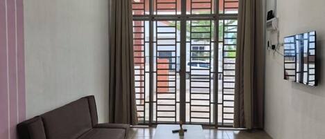 A room with a sofa, a table, and a view through a window with a metal gate.