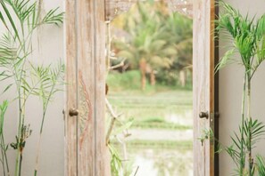 A doorway leading to a lush outdoor area with a view of a green landscape. - Dijero at Umah Bali (Bali)