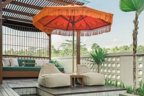 A covered outdoor seating area with a wooden deck, a green sofa, and a red umbrella. - Dijero at Umah Bali (Bali)